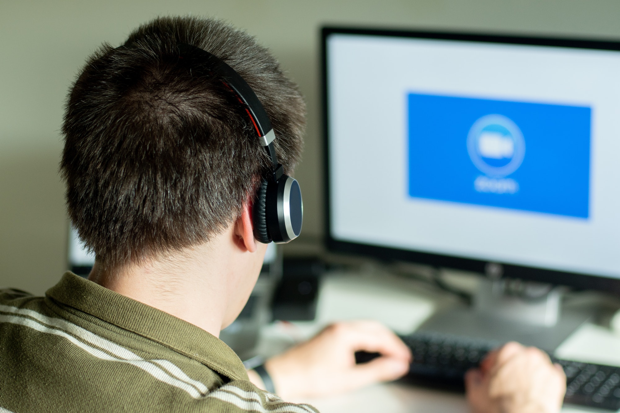 Man with headphones looking on the monitor with zoom cloud meetings logo